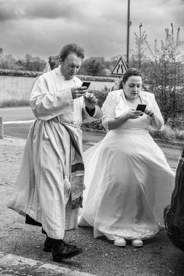 photo mariage noir et blanc prêtre et mariée sur leur téléphone dans le vent