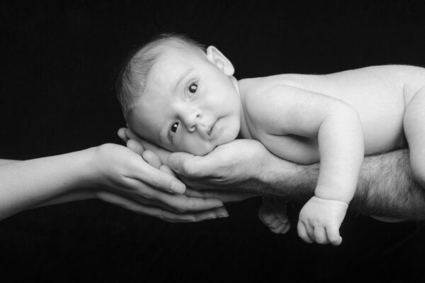 portrait d'un bébé en noir et blanc posant sur les mains de ses parents