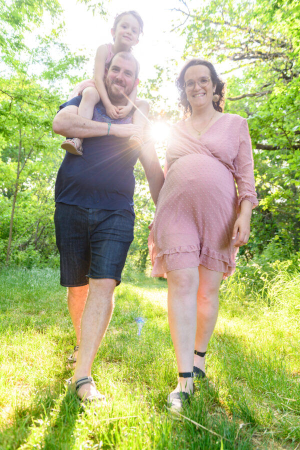 portrait de femme enceinte avec le papa et une jeune fille sur les épaules de son père en forêt