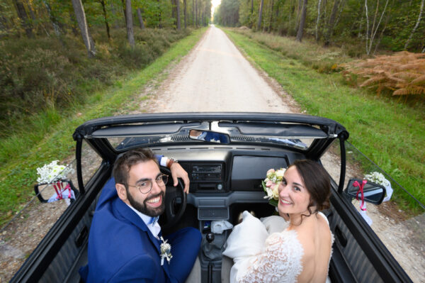 mariés dans une voiture avec un grand chemin de forêt devant