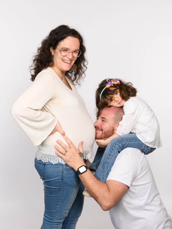 femme enceinte avec le papa faisant un bisous sur le ventre et la petite fille sur ses épaules