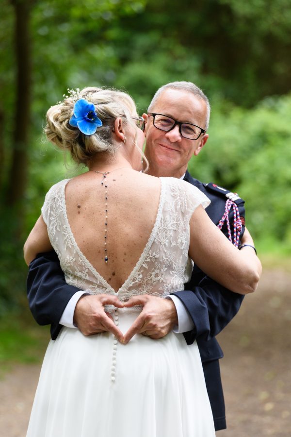 couple de mariés le marié faisant un cœur avec ses doigts devant le dos de la mariée